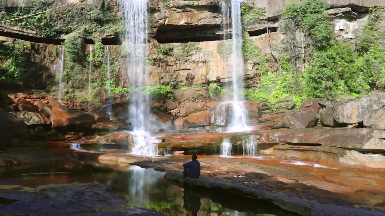 joven disfrutando de la prístina cascada natural que cae desde la cima de la montaña en el día desde un video de ángulo bajo tomado en phe phe fall meghalaya india