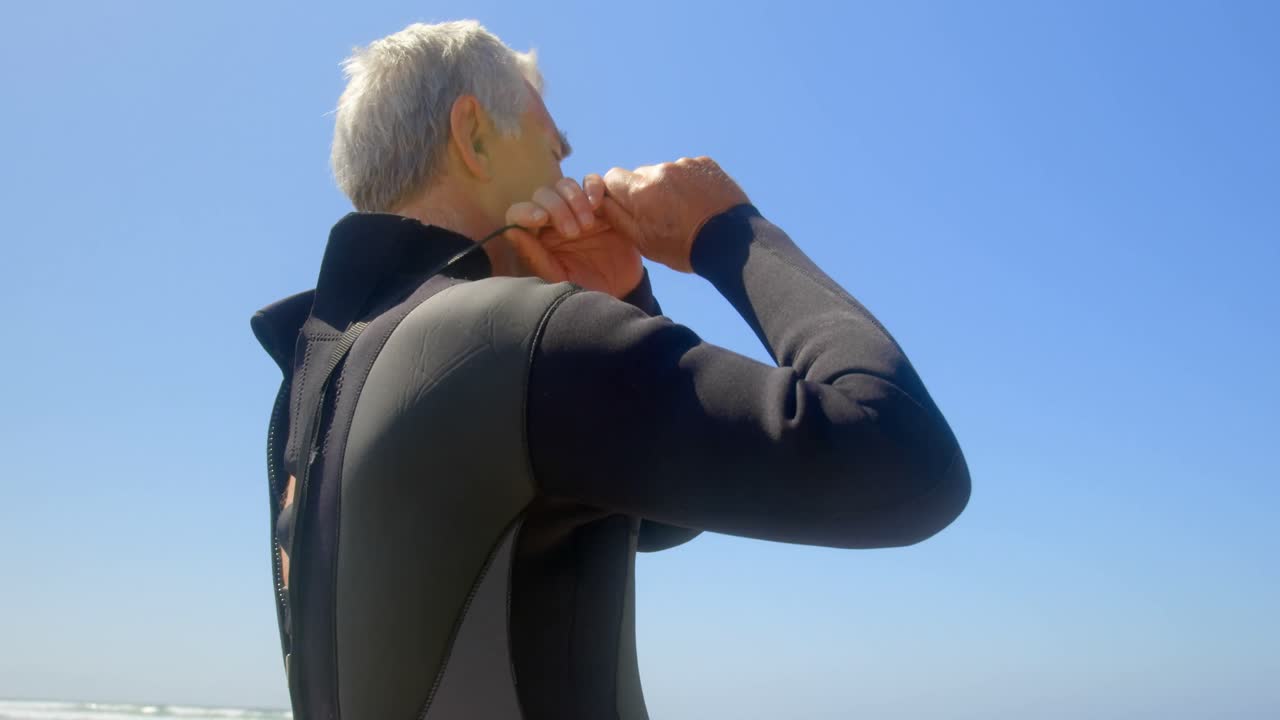 해변 4k에서  ⁇  수복을 입은 활동적인 고위 백인 남성 서퍼의 낮은 각도 뷰