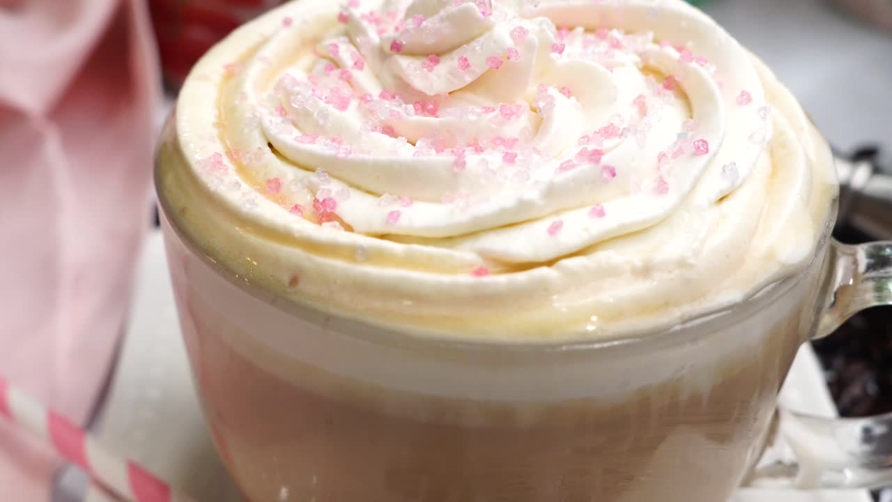 Dessert pink coffee in a mug topped with whipped cream and sugar sprinkles. Delicious and sweet dessert hot coffee in a coffee mug and surrounded by coffee beans.