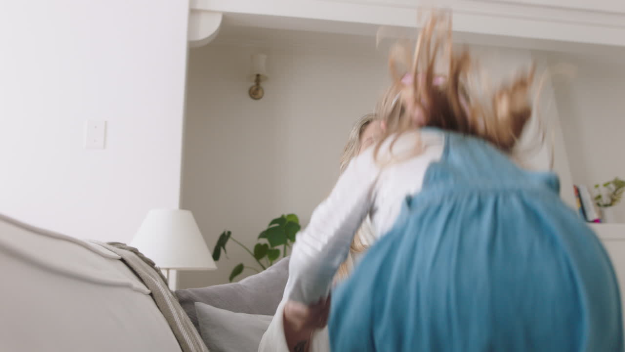 행복한 엄마와 딸이 소파에 뛰어들고 어린 소녀가 엄마와 함께 게임을 하며 즐거운 주말을 함께 즐기고 있습니다. 4k 영상