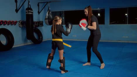 young girl practicing kickboxing with coach in a gym
