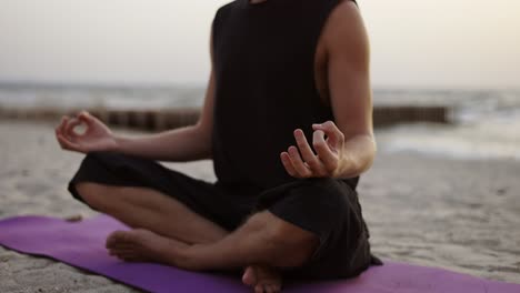 a young man is doing yoga and meditating on a sports mat while sitting during the dawn of the sun. doing a specific exercise. meditation, hands. leisure time, recreation