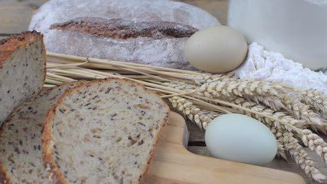 loafs of bread, slices of bread, wheat flour, eggs and ears of grain on wood background. rustic and rural concept. close up. flat lay