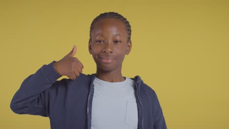 studio portrait of boy smiling and giving thumb up gesture against yellow background