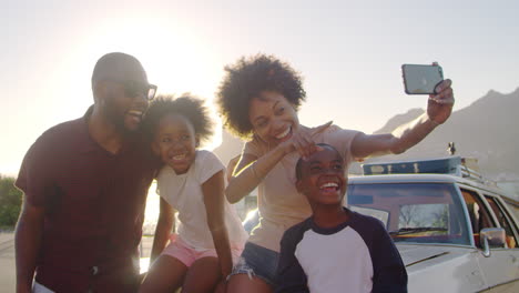 familia posando para una selfie junto al coche empacado para un viaje por carretera