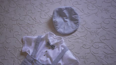 close up of a baby’s baptism outfit with a bow tie and cap on a patterned fabric