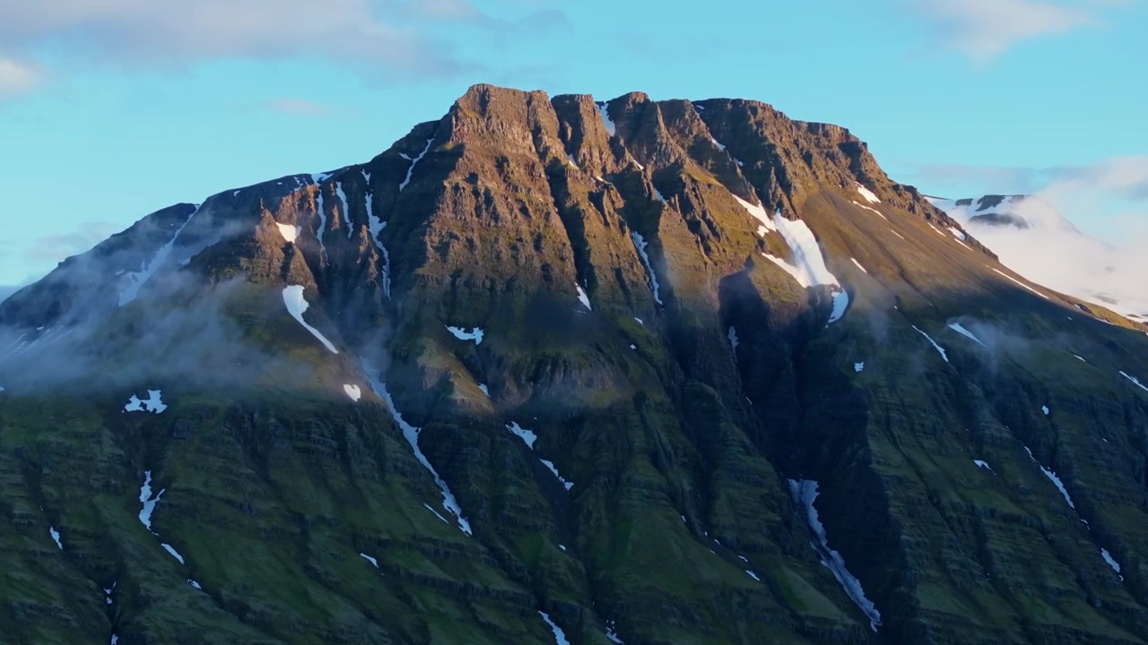 Gylden bjergryg med dvælende sne rejser sig over Reydarfjordur Island