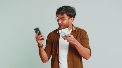 Happy-Indian-man-use-smartphone-rejoicing-game-win-receiving-money-dollar-cash-celebrating-success