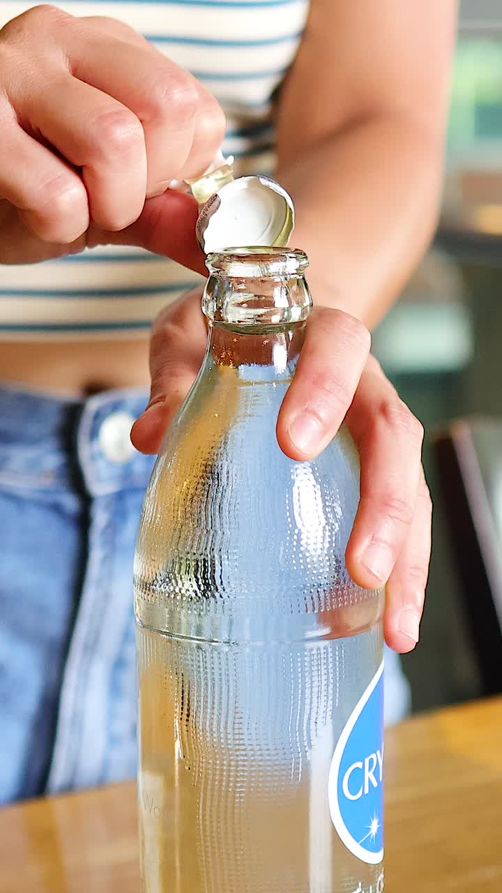 Una persona abre una botella de agua en un ambiente luminoso de restaurante. El atuendo casual y la luz natural crean una atmósfera relajada.