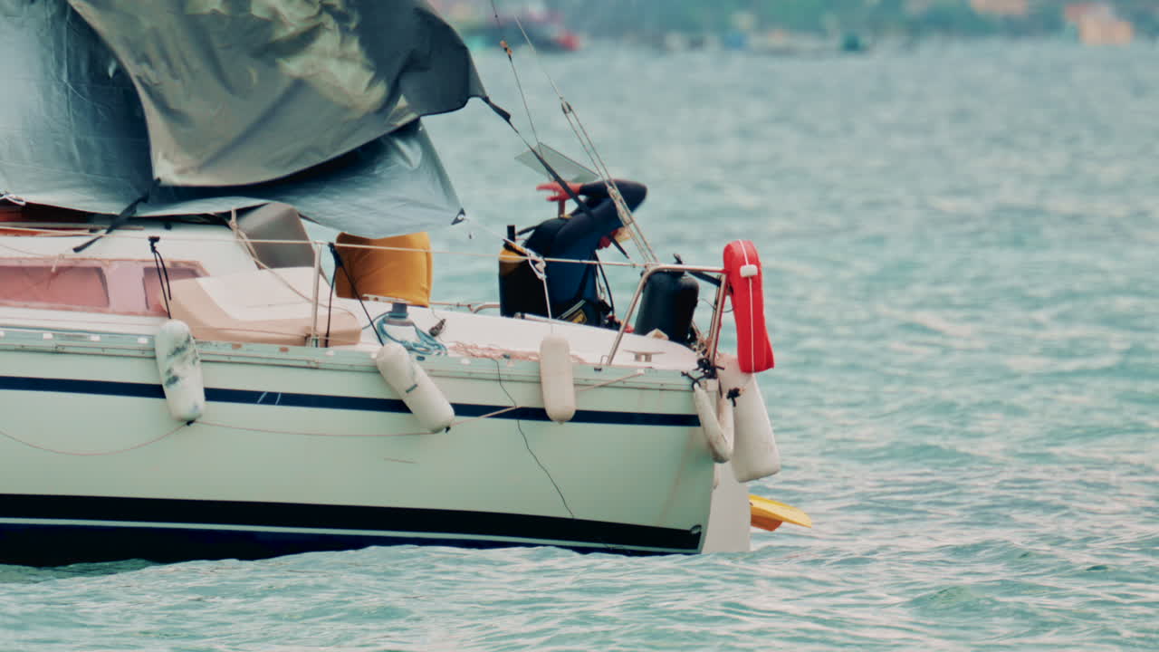 View of a small sailboat rocking on the waves with a lone sailor on deck, diver preparing to jump into sea