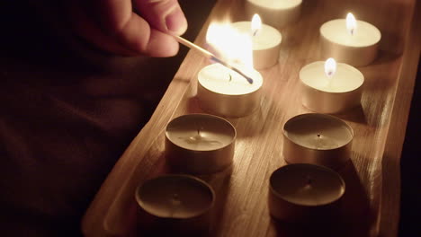 El-Hombre-Enciende-Velas-De-Té-En-Un-Estudio-Oscuro,-Las-Llamas-Parpadean-En-Una-Bandeja-De-Madera