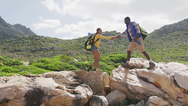 Pareja afroamericana tomados de la mano y caminando sobre las rocas mientras hacen senderismo.