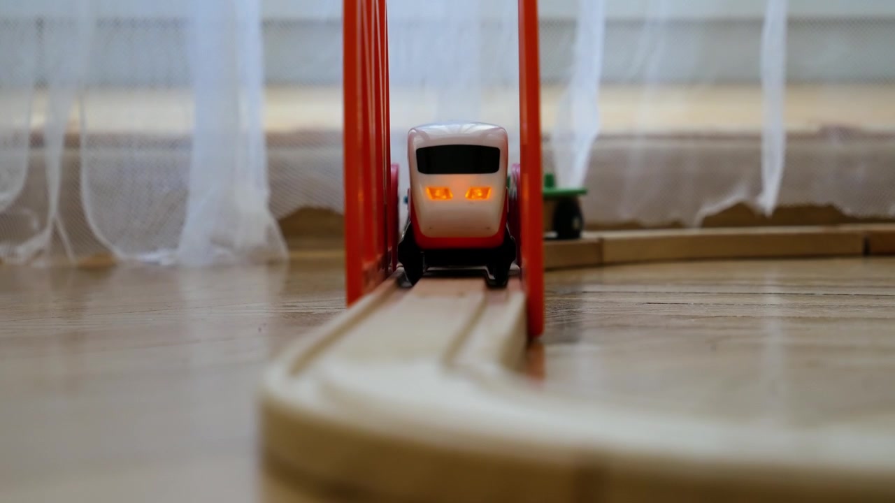 Treno giocattolo di legno che corre su un binario curvo con un ponte rosso all'interno di una casa.