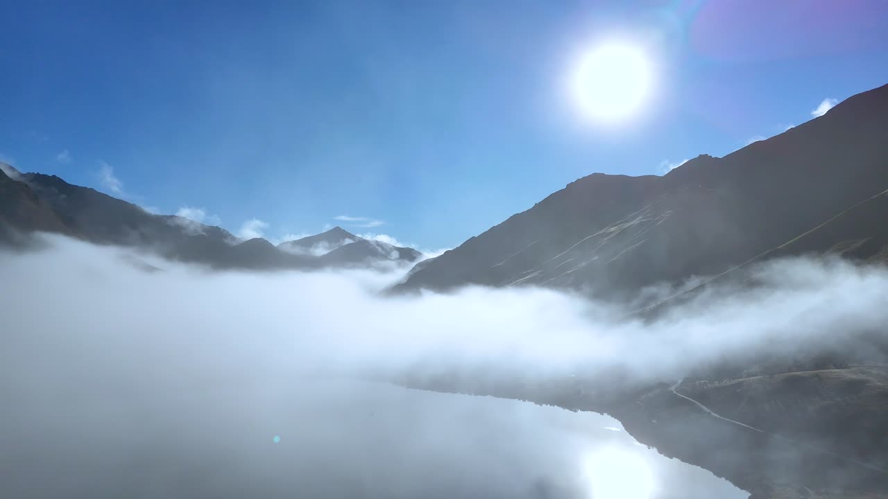 A serene view of fog rolling over mountains and lake under bright sunlight in Queenstown, New Zealand