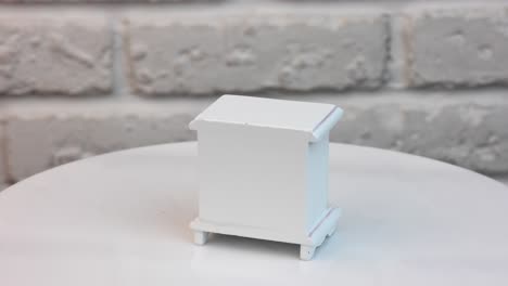 Cute little chest of drawers for doll's house. White wooden piece of interior rotating at the stand. Close up.