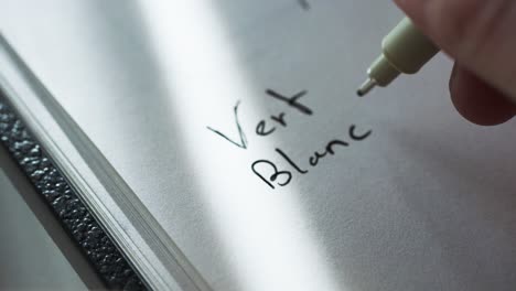 close up shot of a male hands writing names of colors in french on a white paper at daytime