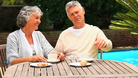 Mature-couple-having-a-snack-by-a-swimming-pool