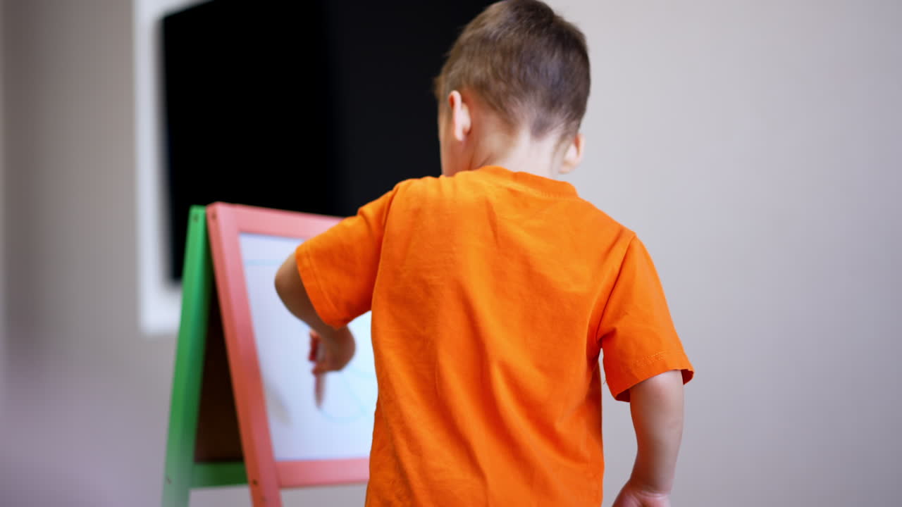 Lovely toddler kid holds a marker in hand. Little baby boy draws on the whiteboard at home.