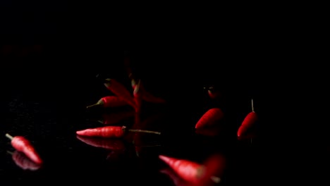 fresh red chilli spices falling on a black background with reflection