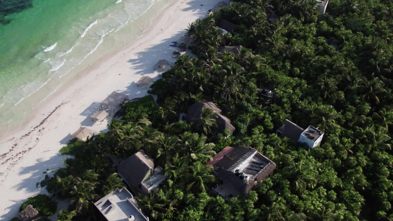 orbita aérea de arriba hacia abajo foto de chozas y cabañas rodeadas de palmeras frente a una playa de arena blanca con aguas cristalinas en tulum, méxico