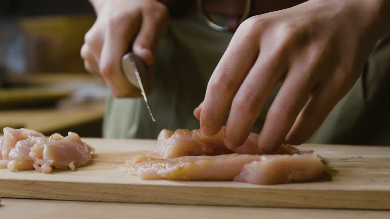 Close-up of hands cutting raw chicken on a wooden board