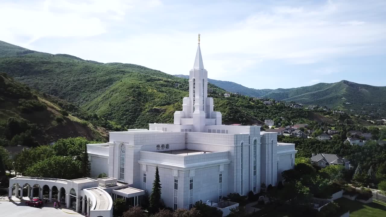 Drone Shot smoothly rotating around the West Side of the Mormon Bountiful Temple with gorgeous mountains and sun flares in the background.