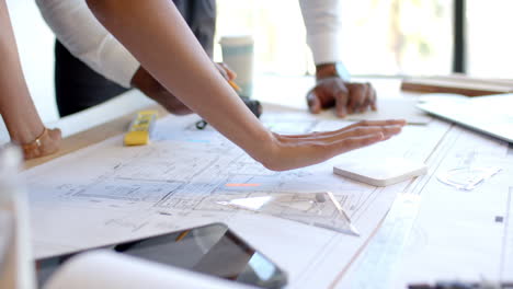 Reviewing architectural blueprints, business professionals collaborating on project plans in office