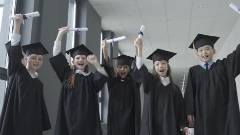 group of happy multiracial preschool students in mortarboard and gown. they are holding their diploma and hugging