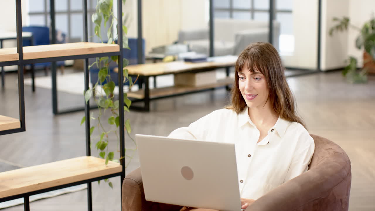 Working on laptop, woman in modern office smiling and focusing on creative writing