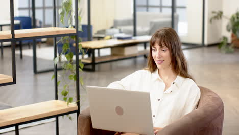 working on laptop, woman in modern office smiling and focusing on creative writing