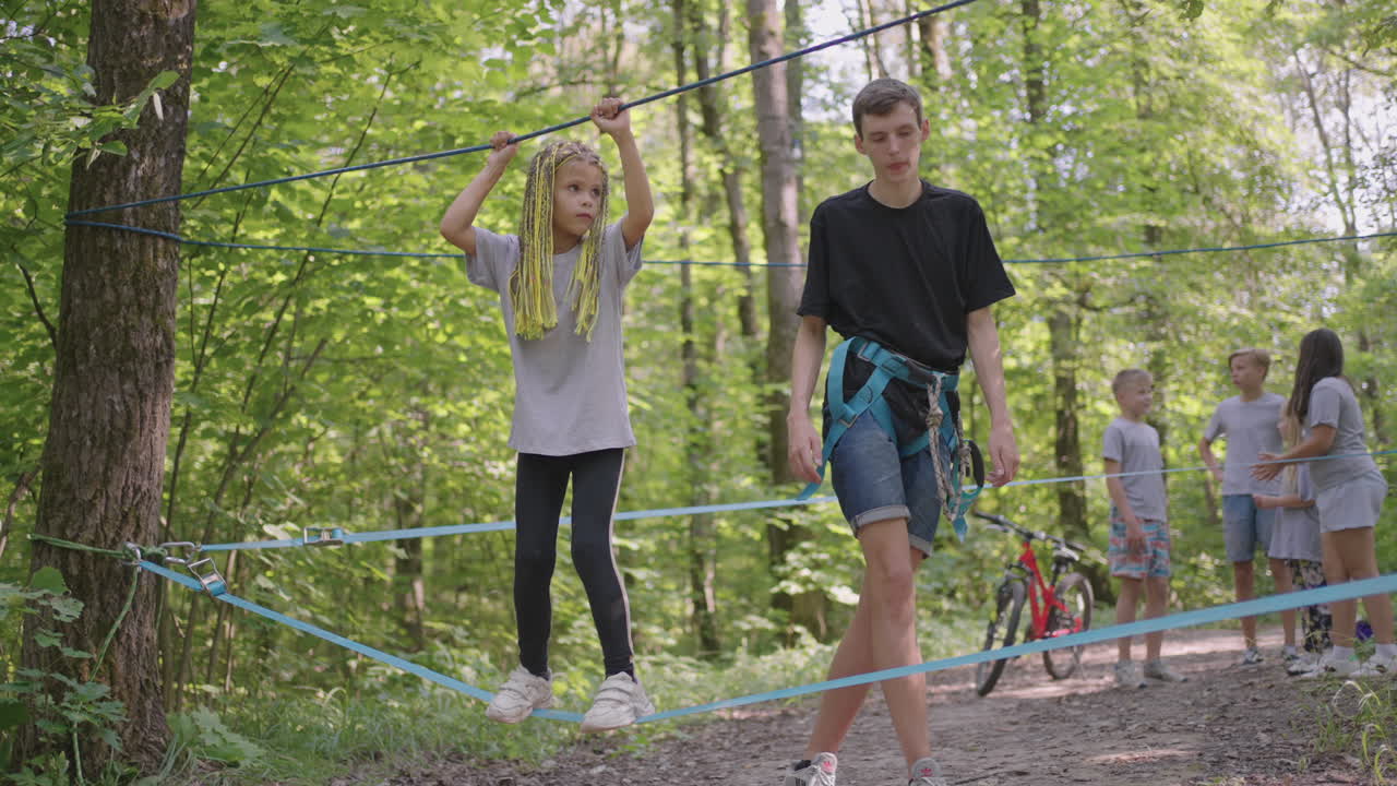 Small girl in climbing equipment in a rope Park. Group of Caucasian children training at boot camp. In the children camp children are taught to overcome obstacles with the help of a rope crossing