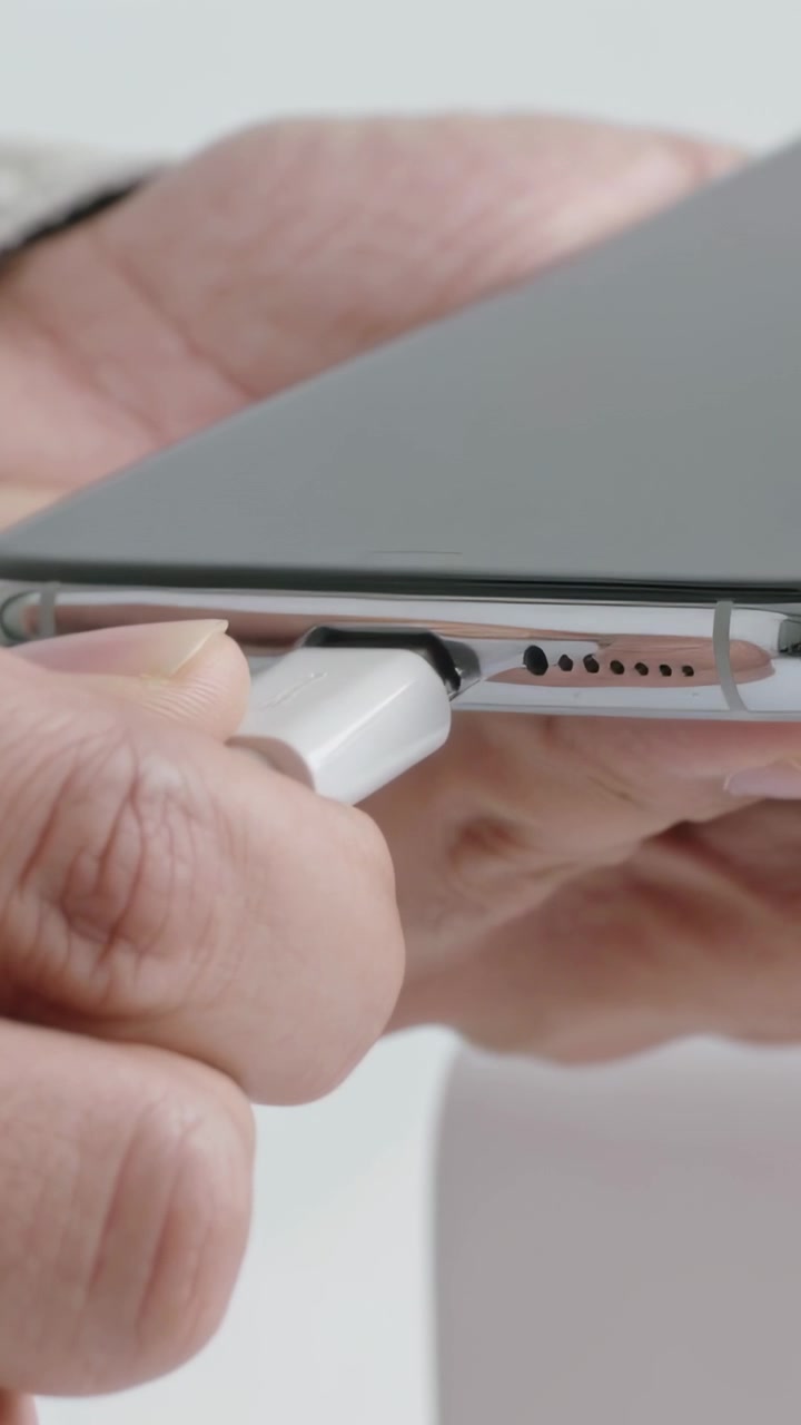 Vertical video: Khaki-cuffed hand testing as USBC plug nearing phone port, plugging pulling at desk