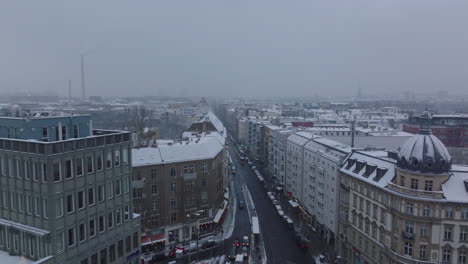 Aerial-footage-of-snowed-roofs-in-town-district.-Forwards-fly-above-cars-driving-on-street-in-city.-Berlin,-Germany