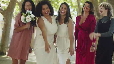 Brides-and-guests-standing-in-line-and-jumping-at-the-same-time,-looking-at-the-camera-and-celebrating-wedding-at-the-park