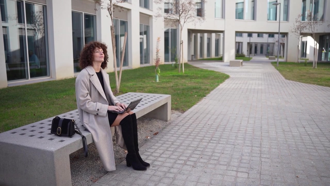 Una donna elegante è seduta e aspetta comodamente su una panchina in un moderno paesaggio urbano.