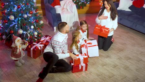 kids and parents with gift boxes at christmas. happy family with little children gathered together on christmas evening near xmas tree enjoy presents. new year celebration. winter holiday event. top view