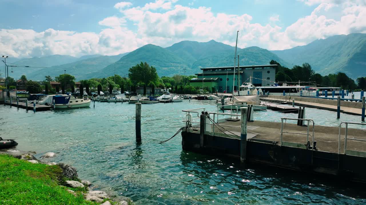 Porticciolo e marina a Lovere sul Lago d'Iseo con barche da diporto bianche e barche a vela ormeggiate. Edificio industriale e uno sfondo montuoso spettacolare sotto la luce intensa del giorno nella regione Lombardia