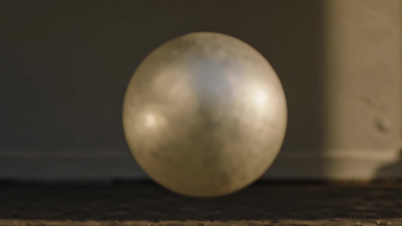 Descending metallic sphere moving toward wooden board in studio, frames advancing, contacting lens