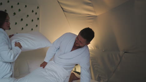 pareja divirtiéndose peleando con almohadas en una habitación acogedora