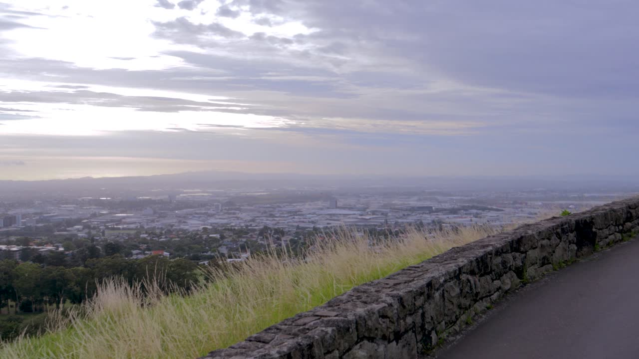 el panorama de la ciudad de auckland visto desde el camino a la cima de una colina de árboles que se convierte en una carretera asfaltada de montaña