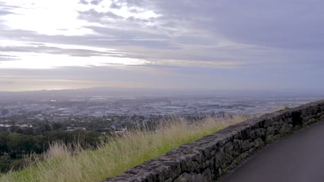el panorama de la ciudad de auckland visto desde el camino a la cima de una colina de árboles que se convierte en una carretera asfaltada de montaña