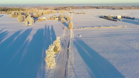 Snow-covered-countryside-roadin-sunset,-aerial-view-flying-over-patchwork-seasonal-rural-landscape-with-long-shadows
