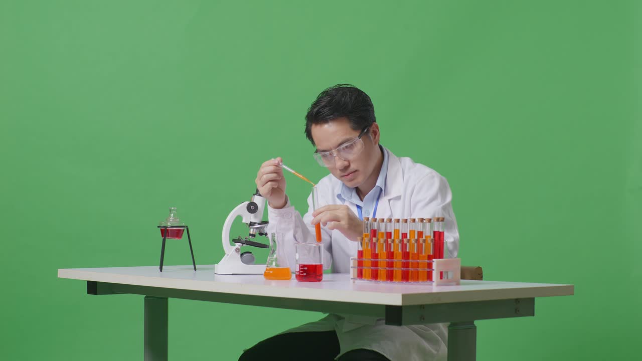 Side View Of Asian Man Scientist Making Experiment With Test Tube And Saying Wow While Working On The Table With Microscope In The Green Screen Background Laboratory