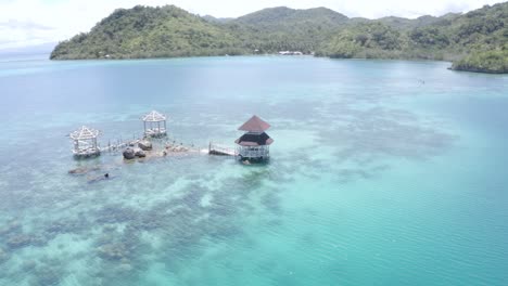 beautiful scenery of a cottage in the middle of crystal clear blue water at the beach in a luxurious tropical island resort in the philippines - travel destination - aerial drone shot, orbiting shot