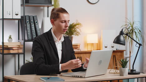 exhausted young businessman using laptop taking off glasses massaging dry irritable eyes at desk