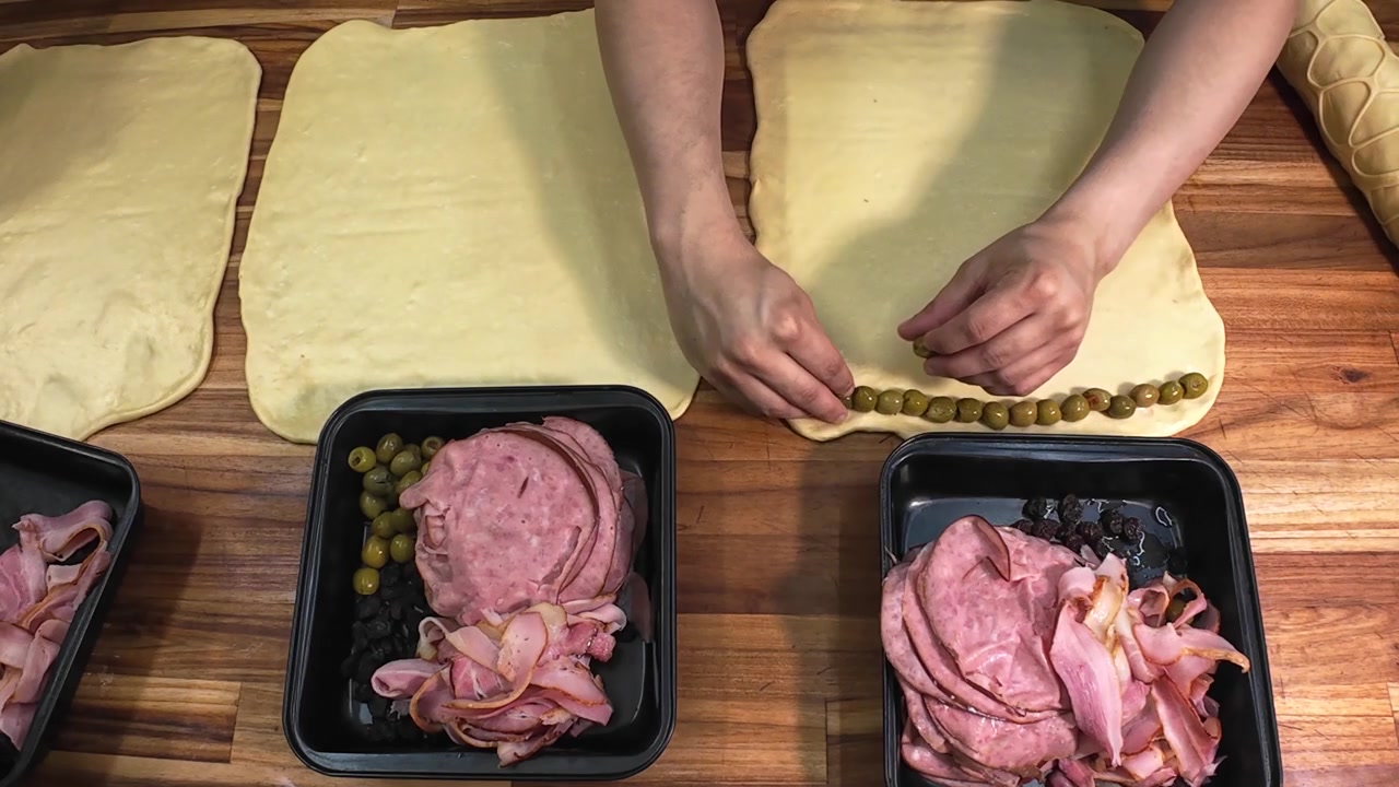 Ovanifrån, medelnära bild av en kock som förbereder traditionell venezuelansk pan de jamón (skinkbröd) på en träbänkskiva.