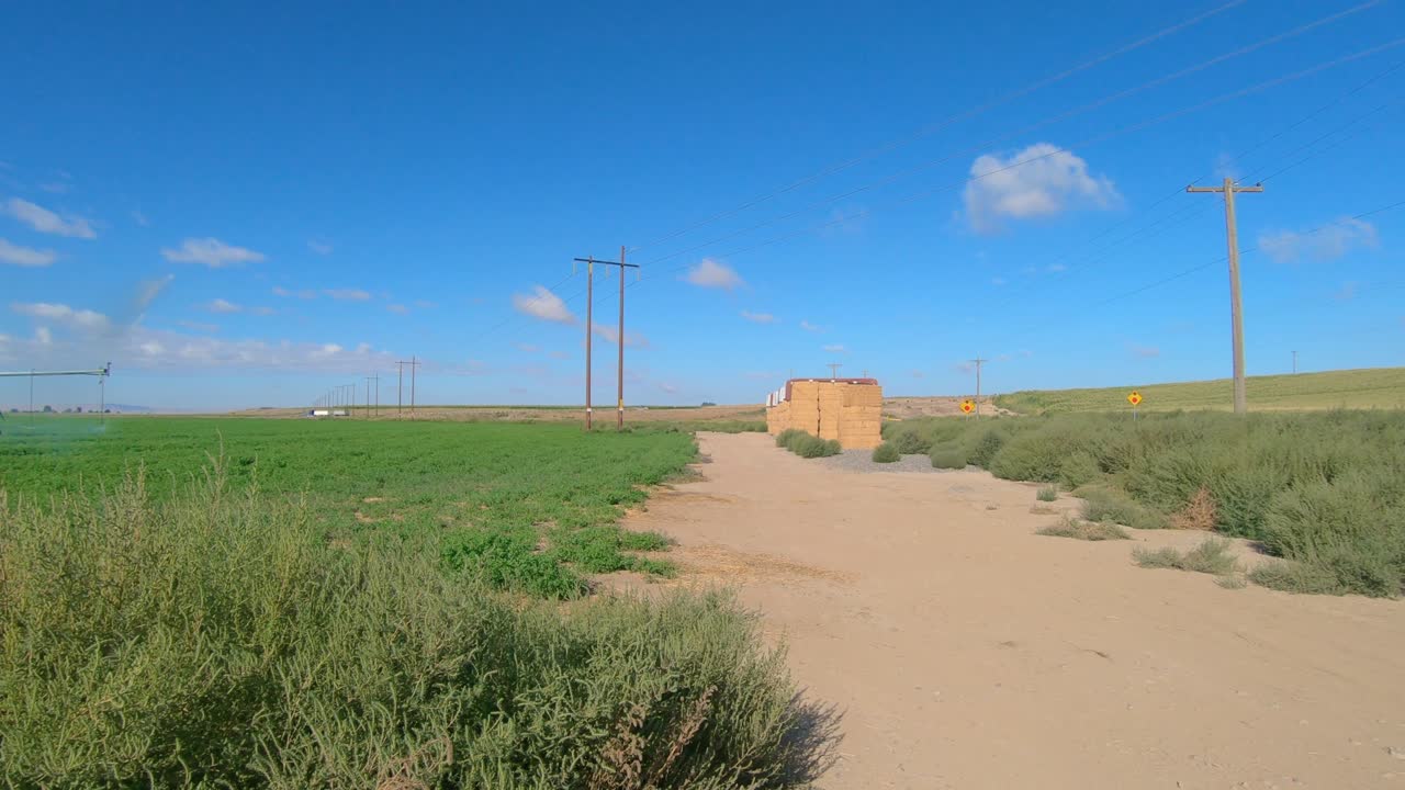 Pan  view of Pivot Irrigation system on an alfalfa field in eastern Washington state; as camera pans the field a Dead End sign and a stack of bales of hay are visible
