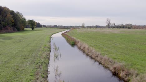 Ascending-areal-drone-footage-of-water-channel-and-vast-farming-fields-with-autumn-colors-taken-at-place-called-Uetz-in-Brandenburg,-Germany