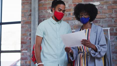 Diversos-Diseñadores-De-Moda-Masculinos-Y-Femeninos-Que-Usan-Máscaras-Faciales-En-Una-Discusión-En-El-Trabajo-Mirando-El-Papel