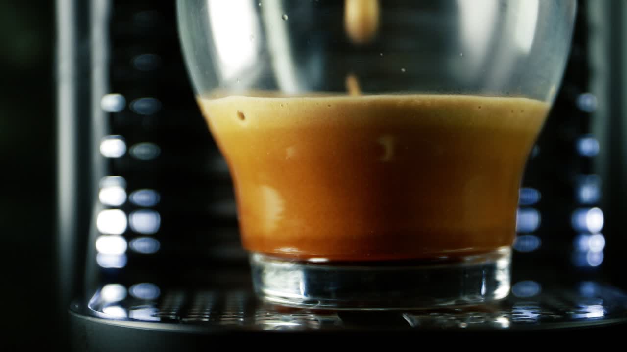 Espresso Glass cup on cafe machine being filled with coffee showing various froth layers shades of brown - static shot